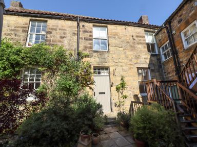 A stone house exterior with wooden door windows and stone steps surrounded by plants and stairs at Beals Yard in Alnwick
