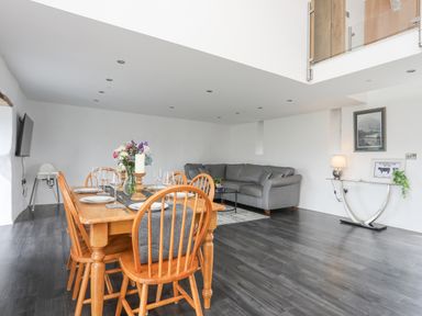 A dining area with a wooden table set with plates and glasses and a gray sofa in the living space at Gwel Y Fenai in Y Felinheli