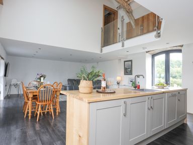 A kitchen island with sink and plants next to a dining table with wooden chairs and a living area with a sofa at Gwel Y Fenai in Y Felinheli
