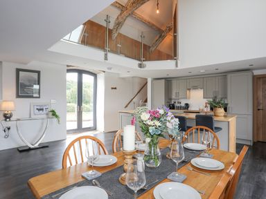 A dining table set with plates glasses and flowers in a kitchen with wooden beams and a glass balcony at Gwel Y Fenai in Y Felinheli