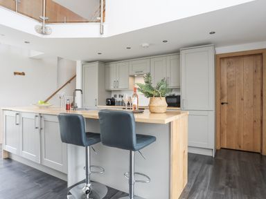 A kitchen with gray cabinets a wooden countertop two bar stools and a wooden door at Gwel Y Fenai in Y Felinheli
