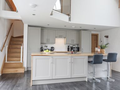 A kitchen with grey cabinets a wooden countertop two bar stools a staircase and kitchen appliances at Gwel Y Fenai in Y Felinheli