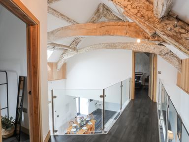 A hallway with wooden beams and glass railing overlooking a dining area at Gwel Y Fenai in Y Felinheli