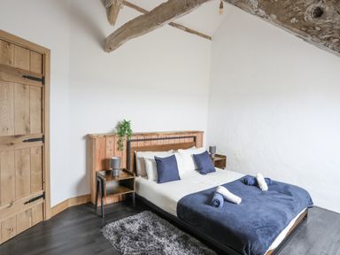 A bedroom with a bed with blue blankets and pillows two bedside tables with lamps wooden door and exposed ceiling beams at Gwel Y Fenai in Y Felinheli