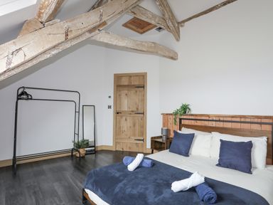 A bedroom with wooden ceiling beams a bed with blue and white linens a wooden door a standing mirror and a black metal clothes rack with hangers at Gwel Y Fenai in Y Felinheli