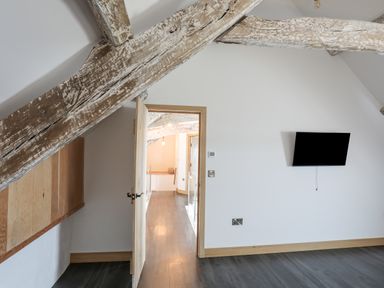 A room with wooden ceiling beams a door leading to a hallway and a wall-mounted television at Gwel Y Fenai in Y Felinheli