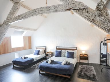 A bedroom with two beds side by side wooden beams and dark flooring at Gwel Y Fenai in Y Felinheli