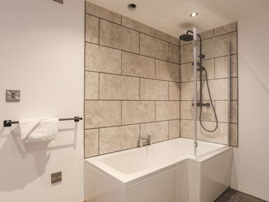 A bathroom with a bathtub shower combo tiled walls and a towel rack with a towel at Gwel Y Fenai in Y Felinheli