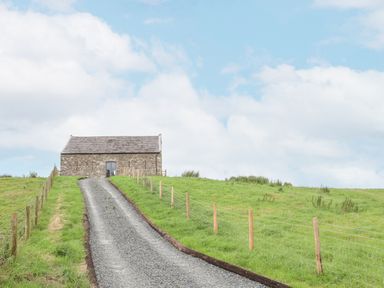 A gravel driveway leading up to a stone building surrounded by green fields at Gwel Y Fenai in Y Felinheli