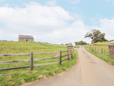 A paved driveway leading to a stone building on a grassy hill with a wooden fence and gate with a private road sign at Gwel Y Fenai in Y Felinheli