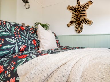 A bed with floral bedding and cream pillows a knitted blanket and a tiger wall hanging at Badgers Rest in Tintagel