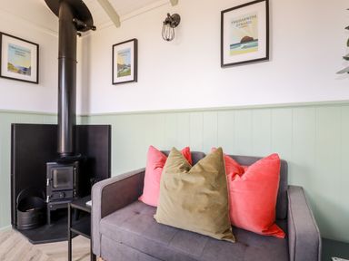 A corner with a wood-burning stove and a gray sofa with colored cushions at Badgers Rest in Tintagel
