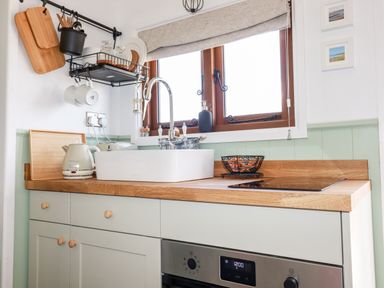 A kitchen countertop with a sink kettle cutting boards and a fruit basket at Badgers Rest in Tintagel
