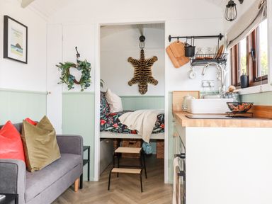 A small living area with a grey sofa and cushions next to a kitchen with a sink and wooden countertop at Badgers Rest in Tintagel