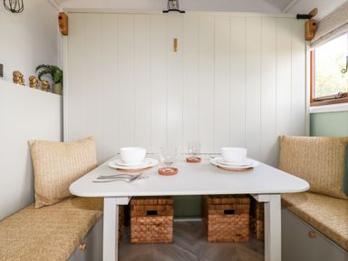 A dining nook with bench seating cushions a white table with place settings and woven storage baskets underneath at Badgers Rest in Tintagel