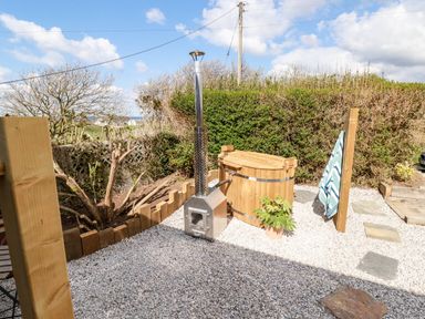 An outdoor area with a wooden hot tub a metal heater a small plant and a towel hanging on a wooden post at Badgers Rest in Tintagel