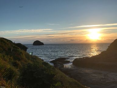 A coastal view with a rocky shoreline and the sun setting over the sea at Badgers Rest in Tintagel