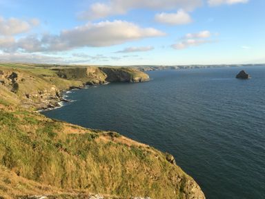 A coastal cliff with grassy land overlooking the sea and a small rock in the water at Badgers Rest in Tintagel