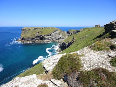 A coastal cliff with grass and rocks overlooking the ocean with a building in the distance at Badgers Rest in Tintagel