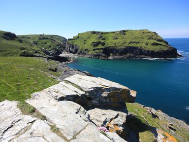 A rocky coastline with green hills and blue water at Badgers Rest in Tintagel