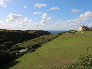 A coastal grassy hillside with a house near the edge and the ocean in the background at Badgers Rest in Tintagel
