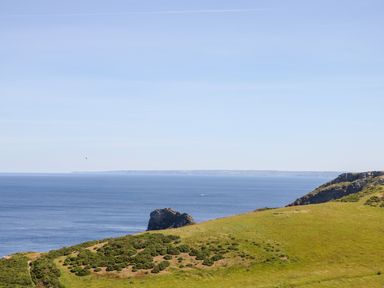 A coastal landscape with grassy hills and a large body of water at Badgers Rest in Tintagel