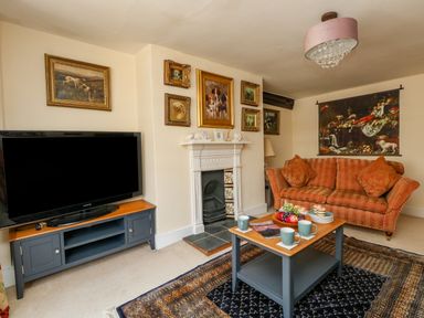 A living room with a television on a stand a fireplace a sofa a coffee table with cups and fruit and paintings on the walls at The Town House in Dorchester