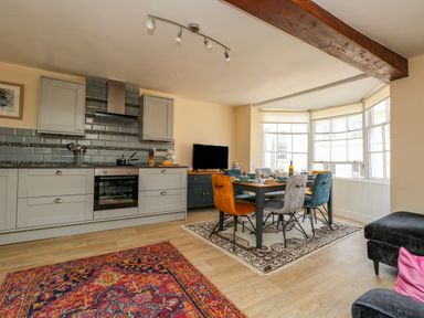 An open kitchen and dining area with a wooden dining table and multicolored chairs by a bay window at The Town House in Dorchester
