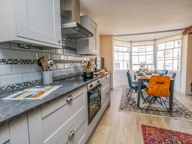 A kitchen with a countertop and cooking utensils next to a dining area with a table set and chairs near windows at The Town House in Dorchester