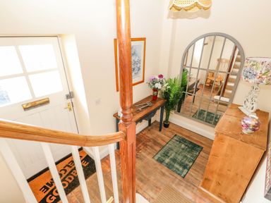 An entryway with a white door a wooden staircase a wooden table with flowers a large mirror and a wooden chest at The Town House in Dorchester