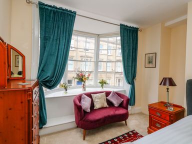 A bedroom with a purple couch under a large window with teal curtains and wooden furniture at The Town House in Dorchester
