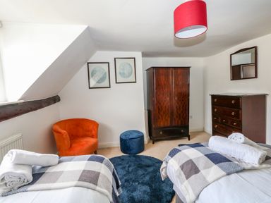 A bedroom with two single beds with plaid blankets an orange chair a blue ottoman a wooden wardrobe and dresser at The Town House in Dorchester