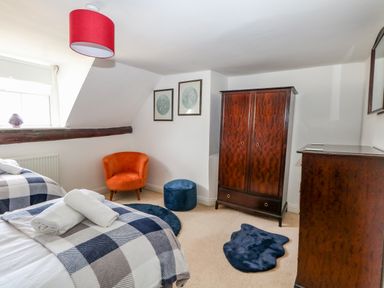 A bedroom with two single beds a wooden wardrobe a wooden dresser an orange chair a blue ottoman and circular and irregular blue rugs at The Town House in Dorchester