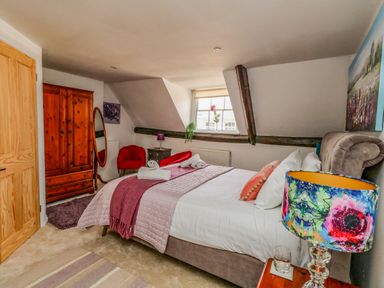 A bedroom with a double bed covered with blankets and pillows a colorful lamp a wooden wardrobe a mirror and red chairs at The Town House in Dorchester