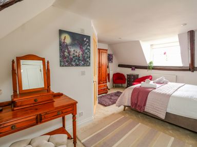 A bedroom with a bed with white and pink bedding a wooden dressing table a wooden wardrobe red chairs and a window at The Town House in Dorchester