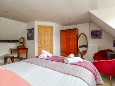 A bedroom with a bed with rolled towels a wooden wardrobe a dressing table and red chairs at The Town House in Dorchester