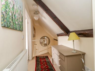 A hallway with a chest of drawers and a lamp on top a red patterned rug on the floor and a painting on the wall at The Town House in Dorchester
