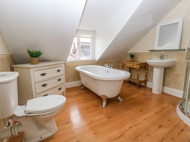 A bathroom with a toilet a freestanding bathtub a pedestal sink a wooden floor and a window at The Town House in Dorchester