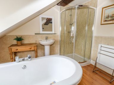 A bathroom with a bathtub sink wooden table with plant glass shower and towel rack at The Town House in Dorchester