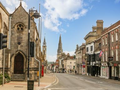 A street view with historic buildings a church with a clock tower and shops displaying Union Jack flags at The Town House in Dorchester