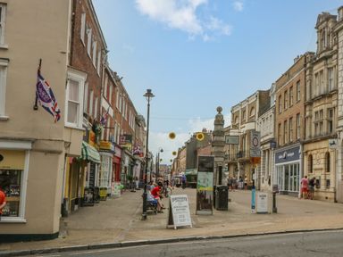 A pedestrian street with shops cafes benches and a stone monument with hanging decorations at The Town House in Dorchester