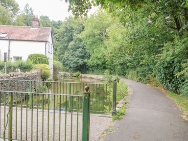 A pathway along a river with green metal gates and a white house with a tiled roof surrounded by trees