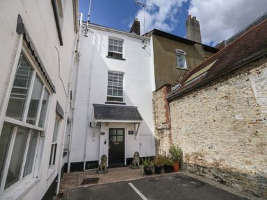A white three-story building entrance with two lion statues and potted plants by a stone wall at The Town House in Dorchester