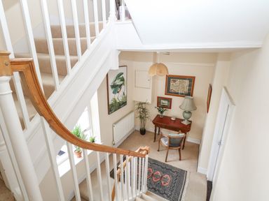 A staircase with white railings overlooking a small seating area with a wooden desk chair and lamp at The Town House in Dorchester