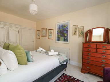 A bedroom with a bed with green pillows a wooden dresser with mirrors and framed artwork on the walls at The Town House in Dorchester