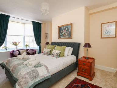 A bedroom with a bed green and floral pillows a wooden bedside table with lamp and a window with green curtains at The Town House in Dorchester