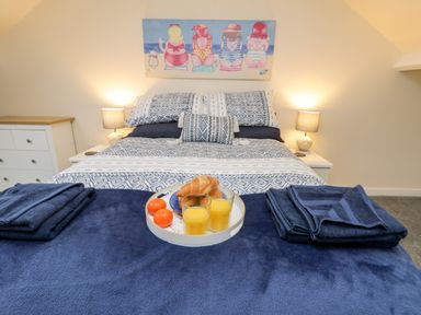 A bedroom with a bed having patterned bedding and towels on it with two glasses of orange juice and croissants at Harbour Hideaway in Whitby