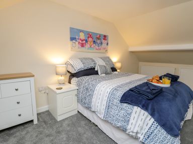 A bedroom with a double bed with patterned bedding bedside tables lamps and a dresser at Harbour Hideaway in Whitby