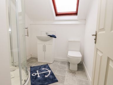 A bathroom with a shower enclosure, a sink cabinet, a toilet, and a blue mat with an anchor design at Harbour Hideaway in Whitby