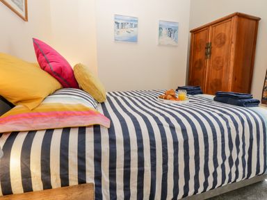 A bedroom with a bed with striped bedding and colorful pillows a wooden wardrobe and framed paintings on the wall at Harbour Hideaway Whitby